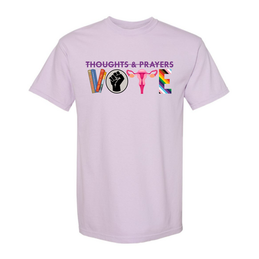 The image shows an Orchid (a light purple) Shirt and features a graphic that is rectangular. At the top in dark purple letters are the words Thoughts and Prayers with a line struck through them. Below is the word VOTE. The V is formed by four banned books, the O is a black circle with a black raised fist on a gray background representing black lives matter. The T is uterus with fallopian tubes and ovaries in pink. The E is Rainbow striped to represent the LGBTQIA+ community. 