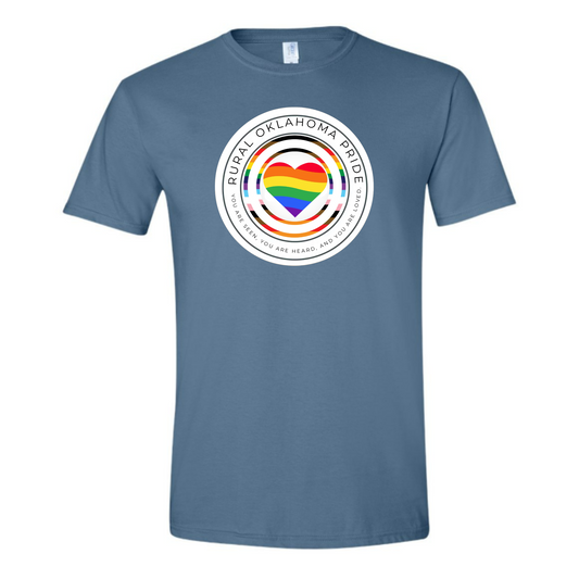 An indigo blue shirt is shown. On it is the rural oklahoma pride logo. The logo has Rural Oklahoma Pride written along the top half of a white circle. The bottom half reads You are seen You are Heard and You are Loved there is the outline of another circle the colors of the Daniel Qasar pride flag with an identical outline slightly smaller inside of it. At the very center of the design is a heart that is colored with waves of color that form the rainbow. 