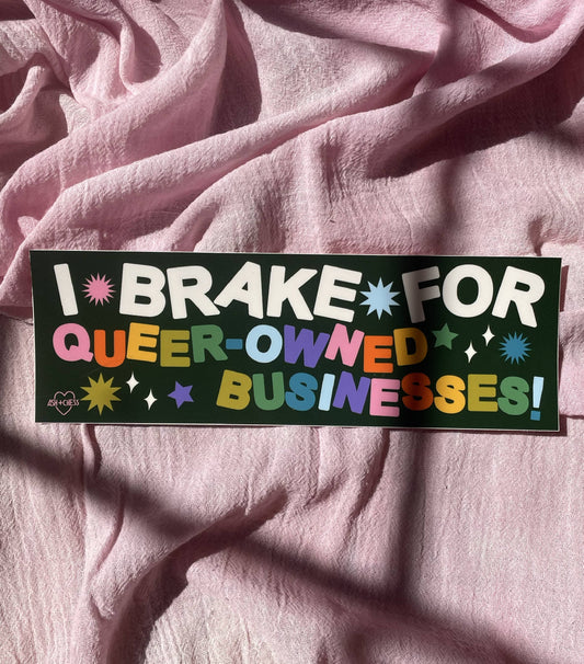 This sticker says I Brake For Queer-Owned Businesses with an exclamation mark at the end. The first three words are white and each of the other words has letters that alternate in color between pink, orange, yellow, two shades of green, blue, and purple. The background of the sticker is dark colored and there are various stars and burst shapes in the&nbsp; blank space.